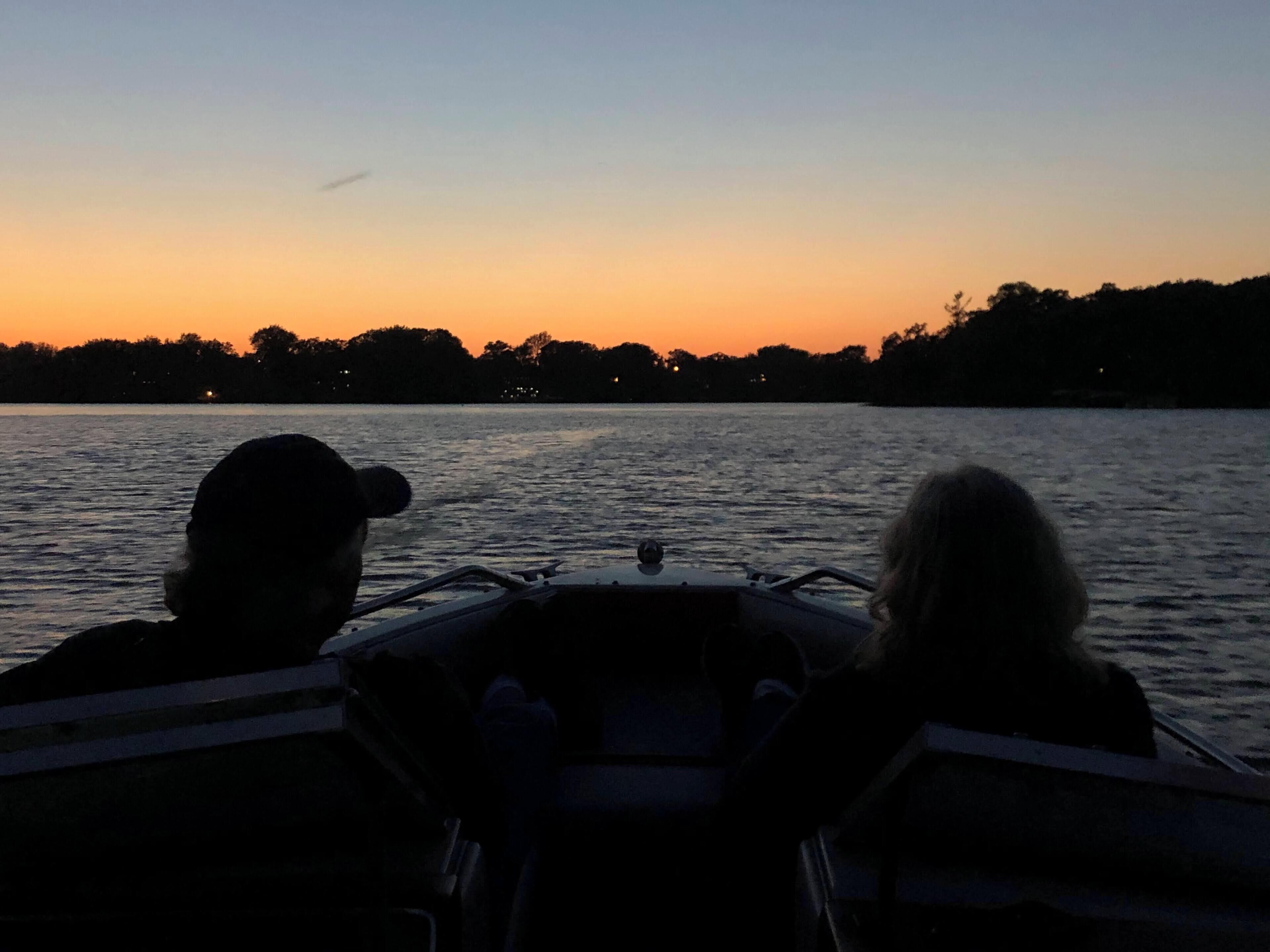 Two people on a boat with a view of a sunset over water.