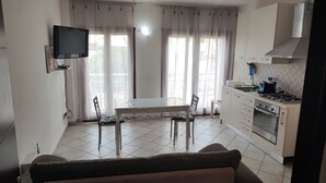 A kitchen with a dining table and chairs, a TV mounted on the wall, and a sofa in the foreground. - Holiday House iolo (Prato)
