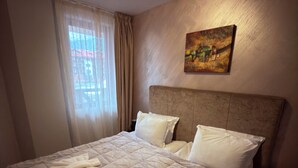 Ein ordentlich bezogenes Bett mit einem gepolsterten Kopfteil, ein Bild an der Wand und ein Fenster mit Vorhängen.