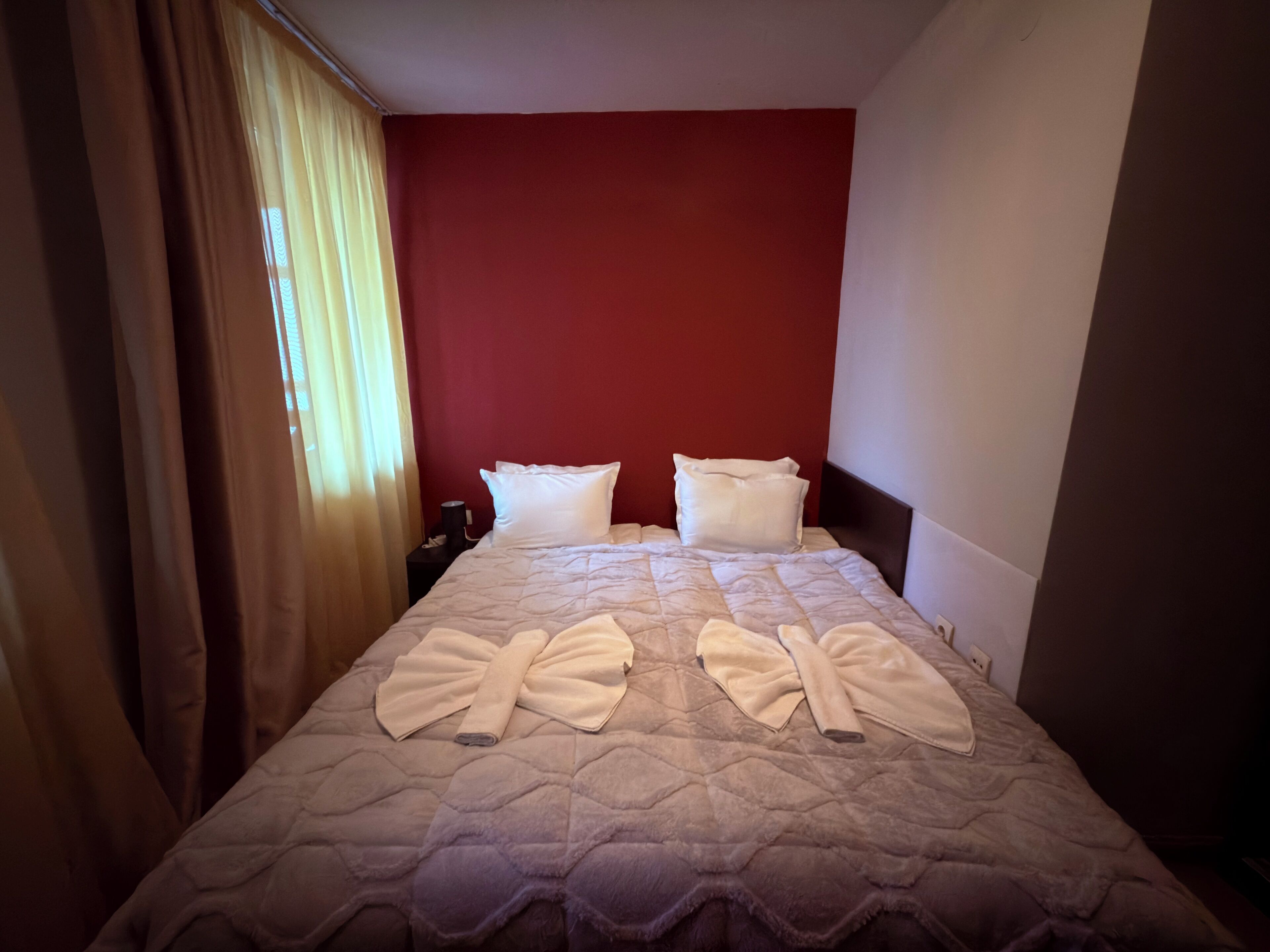Una habitación de hotel con una cama, paredes rojas y una ventana con cortinas.
