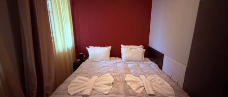 Una habitación de hotel con una cama, paredes rojas y una ventana con cortinas.