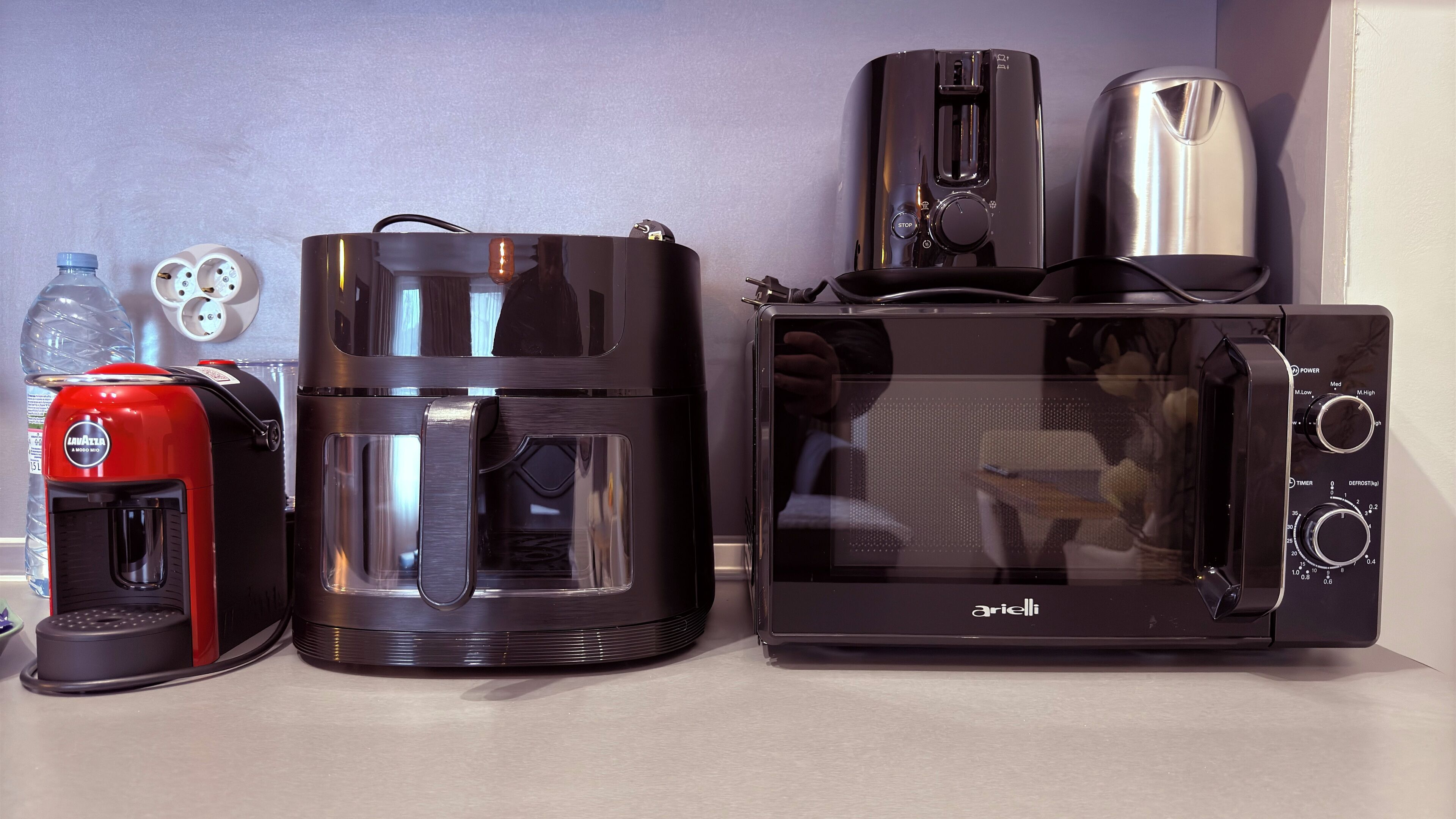 A kitchen with a coffee maker, a coffee machine, a toaster, and a microwave.