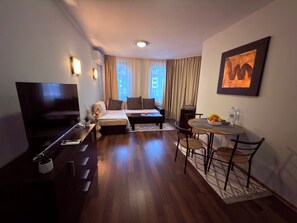 A compact hotel room with a sofa bed, a small dining table, a TV, and a painting on the wall. - Florimont Heights Apart Complex (Bansko)