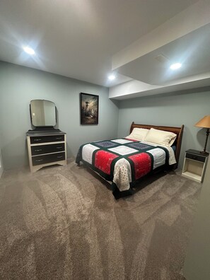 A bedroom with a bed, dresser, mirror, painting, and a lamp.