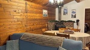 A cozy room with a wooden ceiling, a blue sofa, a table with chairs, and a fireplace. - Large Family Home at Deka Lake (Lone Butte)