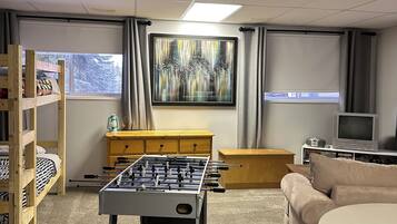 Una habitación acogedora con mesa de fútbol, un sofá, un televisor y un cuadro en la pared.