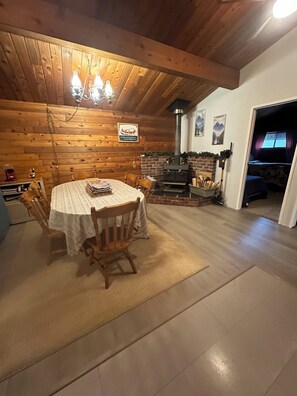 A cozy dining area with a wooden ceiling, a round table with chairs, a brick fireplace, and a sign on the wall.