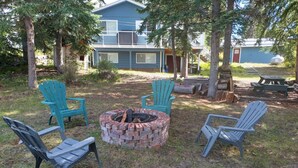 A backyard with a fire pit, four Adirondack chairs, and a house in the background. - Large Family Home at Deka Lake (Lone Butte)