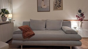 A living room with a sofa, a potted plant, a lamp, and wall art.