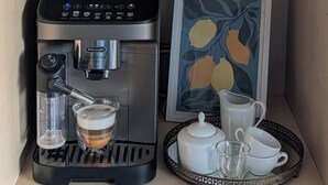 A coffee machine, a glass of coffee, a potted plant, a framed certificate, and a tray with cups and a teapot.