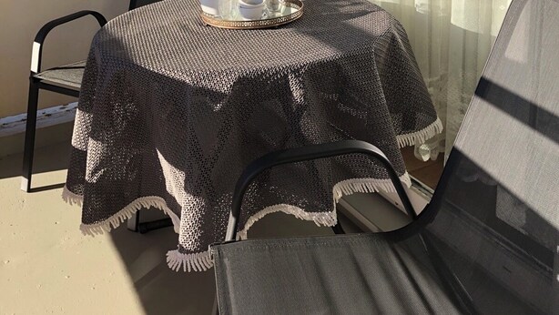 A balcony with a table covered by a knitted tablecloth, a chair, and a glass door with curtains.