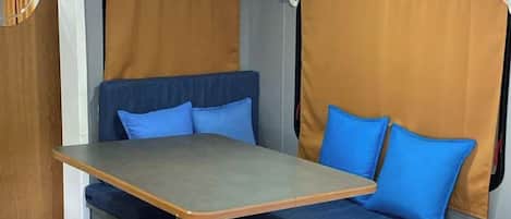 Una habitación pequeña con una mesa y un banco, un espejo y cortinas.