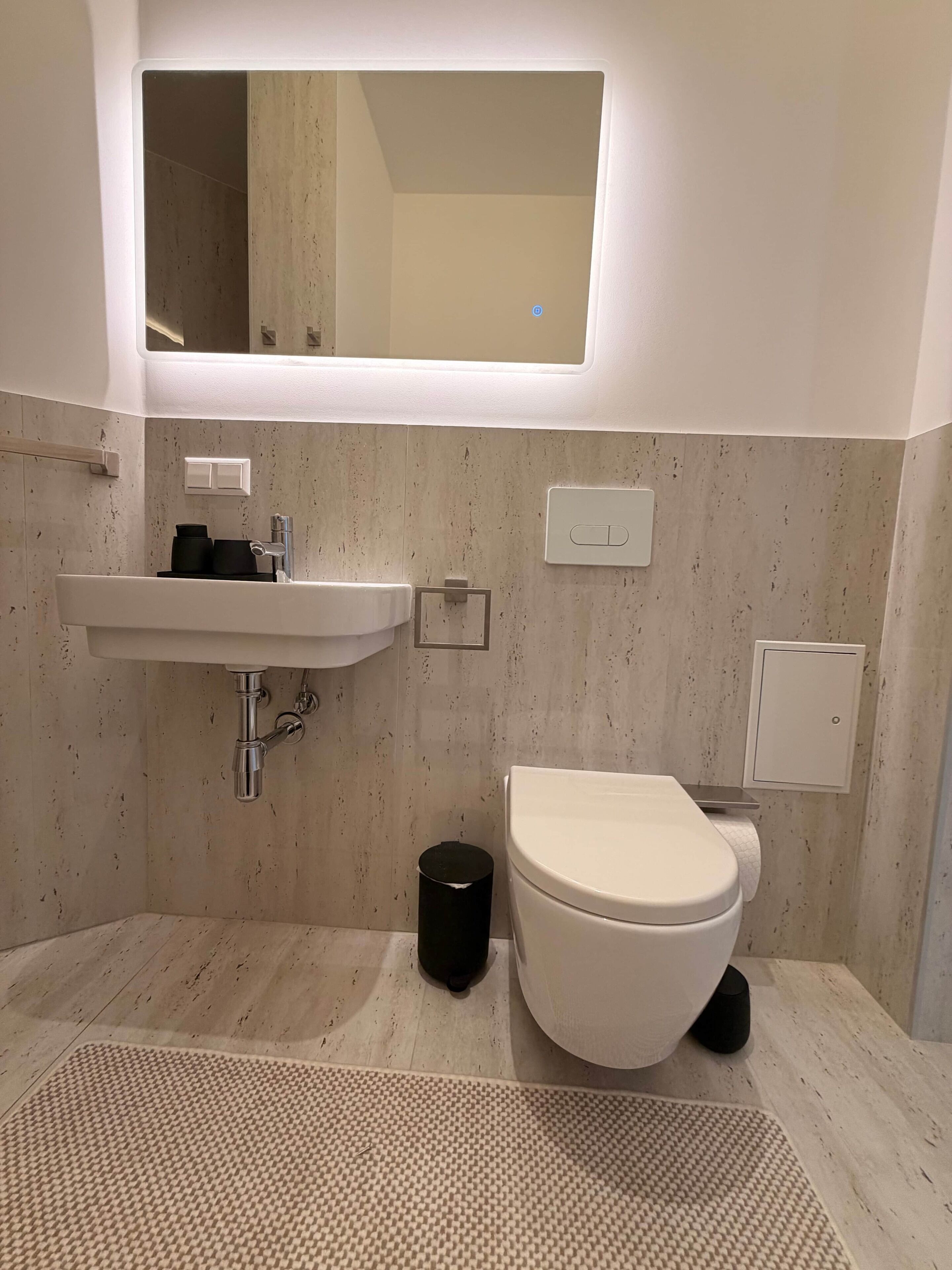 Een moderne badkamer met een witte wastafel, toilet en spiegel boven de wastafel.