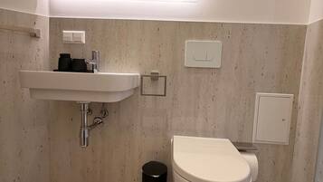 Een moderne badkamer met een witte wastafel, toilet en spiegel boven de wastafel.