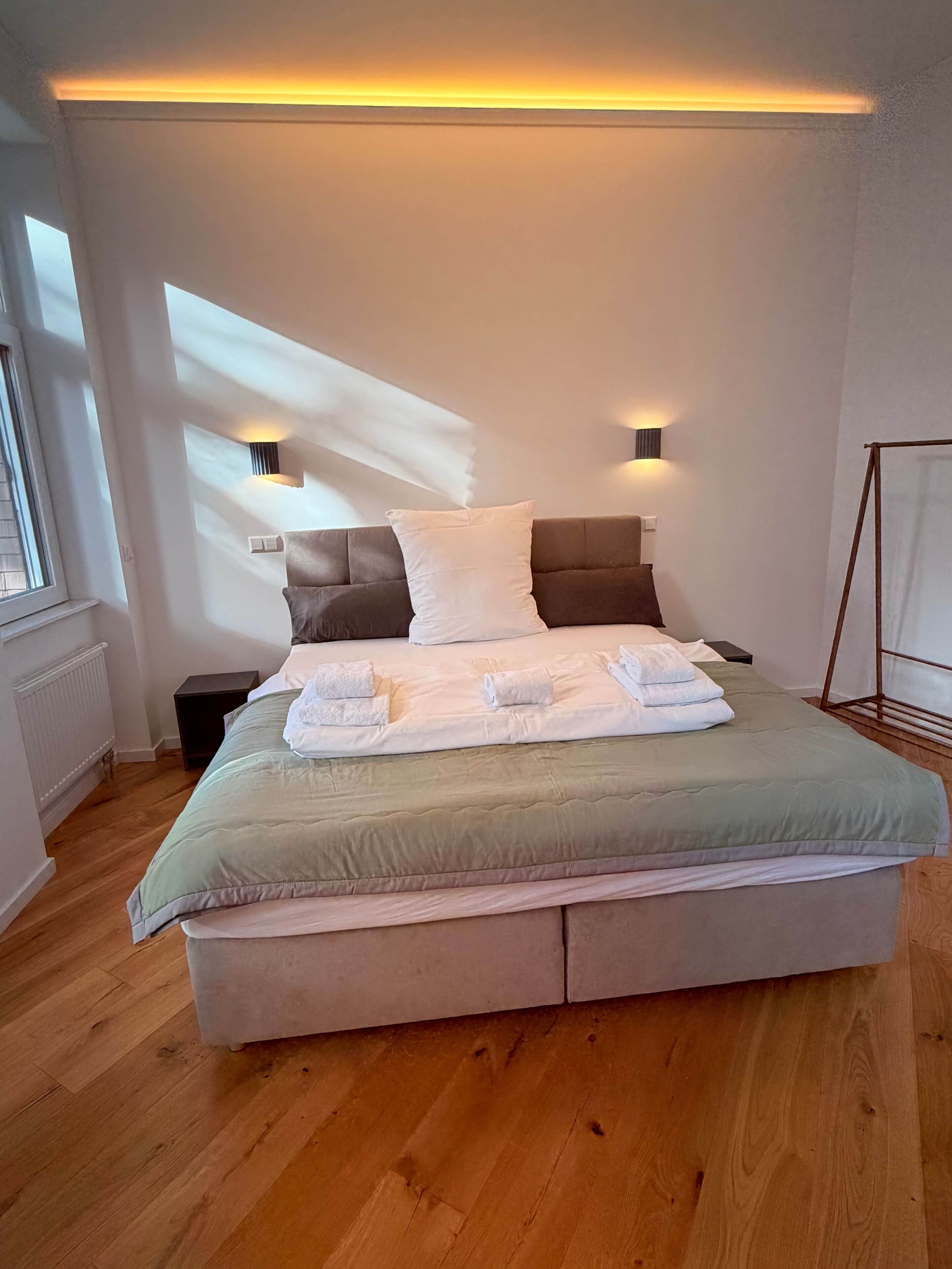 Ein modernes Schlafzimmer mit einem großen Bett, zwei Nachttischlampen und Blick zum Himmel durch das Fenster.