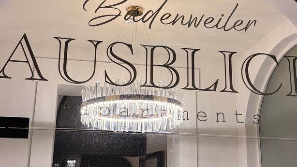 L’entrée d’un hôtel, avec l’inscription « Bodenweiler AUSBLICK » et un lustre.