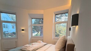 Une chambre moderne avec un grand lit, deux fenêtres et un luminaire au plafond.