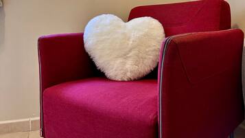 A red chair with a white heart-shaped pillow, a window with a view of greenery, and a poster on the wall titled "Flower Gallery".