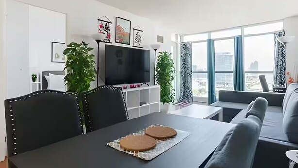 Ein modernes Wohnzimmer mit einem Esstisch, schwarzen Stühlen, einer Couch und einem Fernseher.