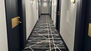 A hotel corridor with doors on both sides, a patterned carpet, and wall-mounted light fixtures.