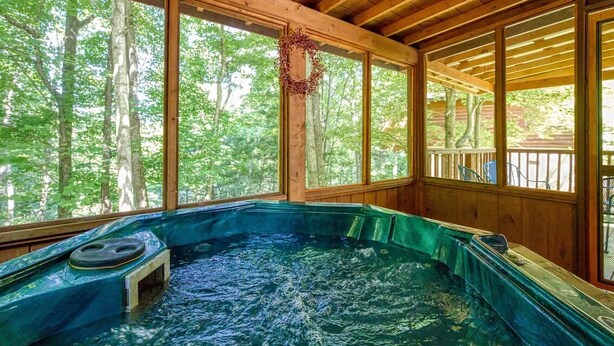 Un jacuzzi en una cabaña de madera con ventanas amplias y vistas al bosque.