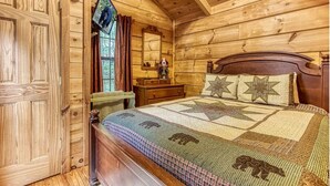 Un dormitorio de cabaña de madera con cama, cómoda, espejo y ventana con cortinas.