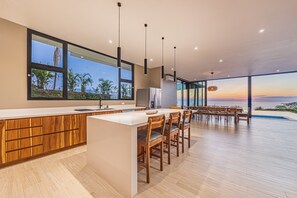 A modern kitchen with a large island, wooden cabinets, and a view of the ocean. - Professional CHEF Included! Oceanview 6 Bedrooms Villa, Pool, Heated Hot Tub (Puntarenas Province)
