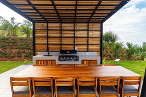 An outdoor kitchen with a large wooden table and chairs, a built-in grill, and a stone countertop. - Professional CHEF Included! Oceanview 6 Bedrooms Villa, Pool, Heated Hot Tub (Puntarenas Province)