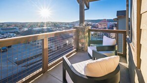 A balcony with a view of a parking lot and buildings, a stone pillar, and a chair with a cushion. -  New Modern Downtown Penthouse Condo with undercover parking (Flagstaff)