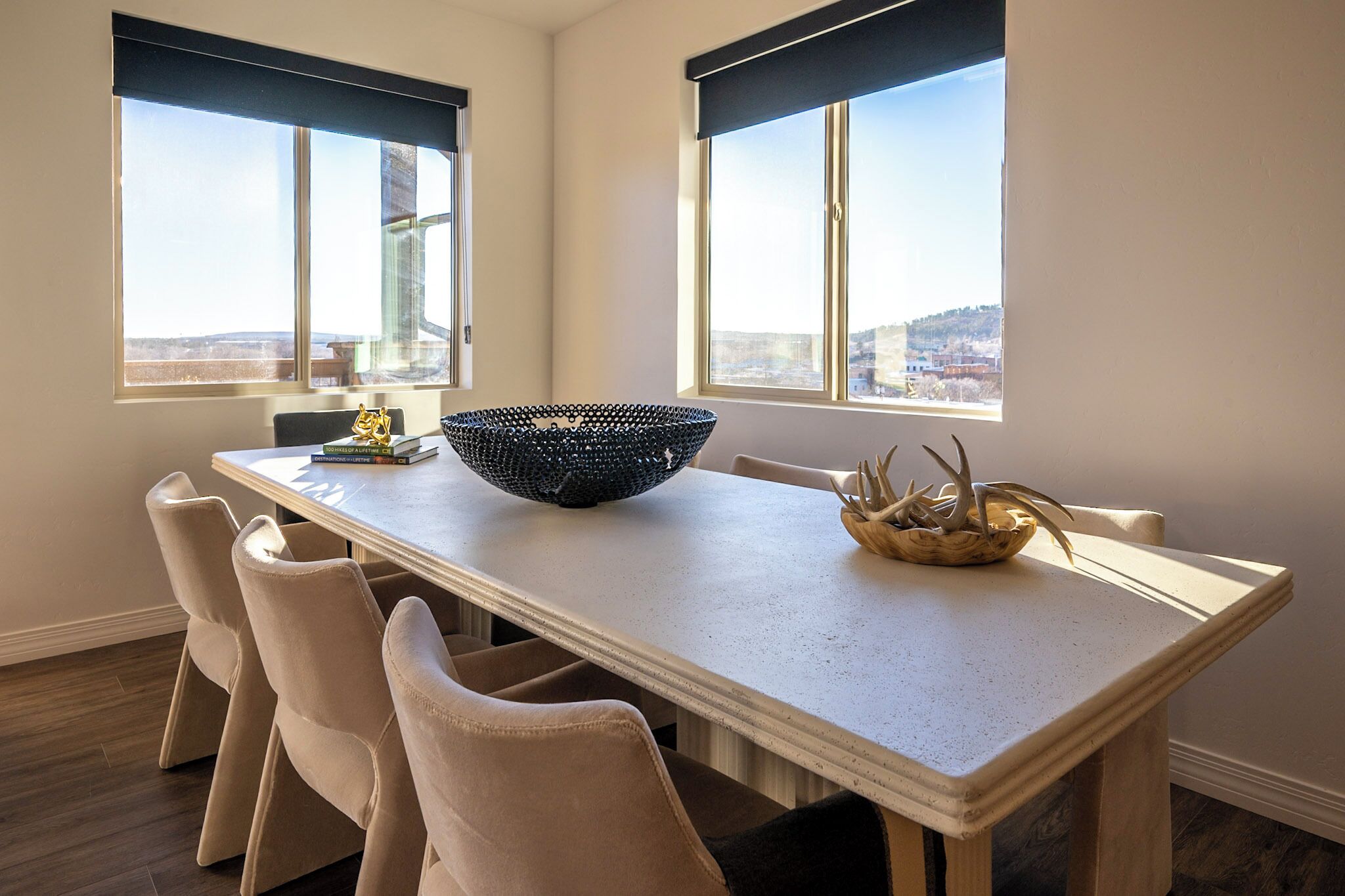 A dining area with a long table, beige chairs, a black woven bowl, and a small plant.