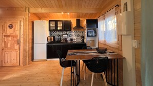 Cocina compacta con armarios de madera, un refrigerador, un microondas y una zona de comedor con sillas.