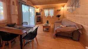 Interior acogedor de una cabaña con una mesa de comedor de madera, sillas, un sofá y un televisor en un estante.