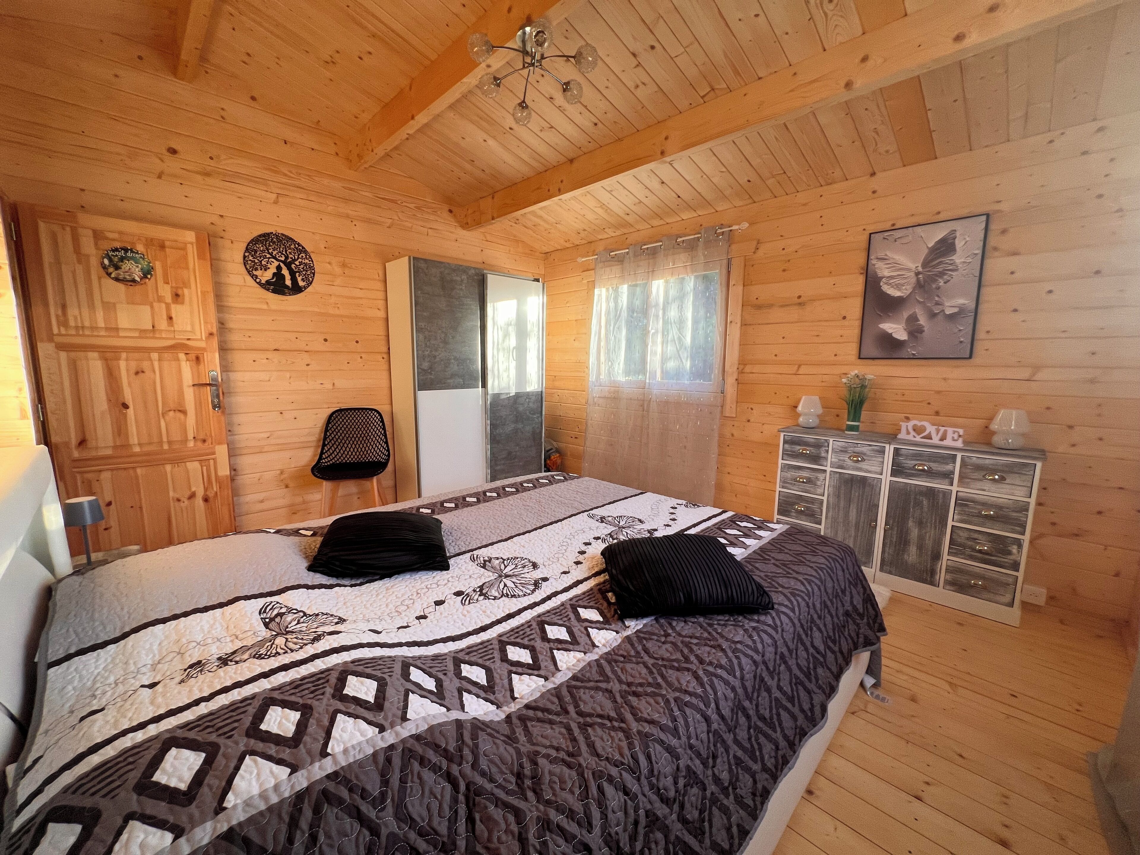 Un dormitorio de cabaña de madera con una cama, un tocador, una silla y una puerta.