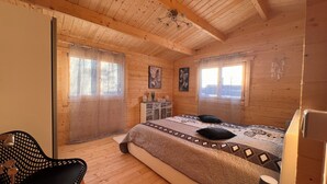 Un dormitorio de cabaña de madera con cama, una silla, un tocador y una ventana.