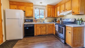 A kitchen with wooden cabinets, a white refrigerator, a microwave, a dishwasher, a stove, and a sink. - 8th St Retreat: Loveland Comfort (Loveland)