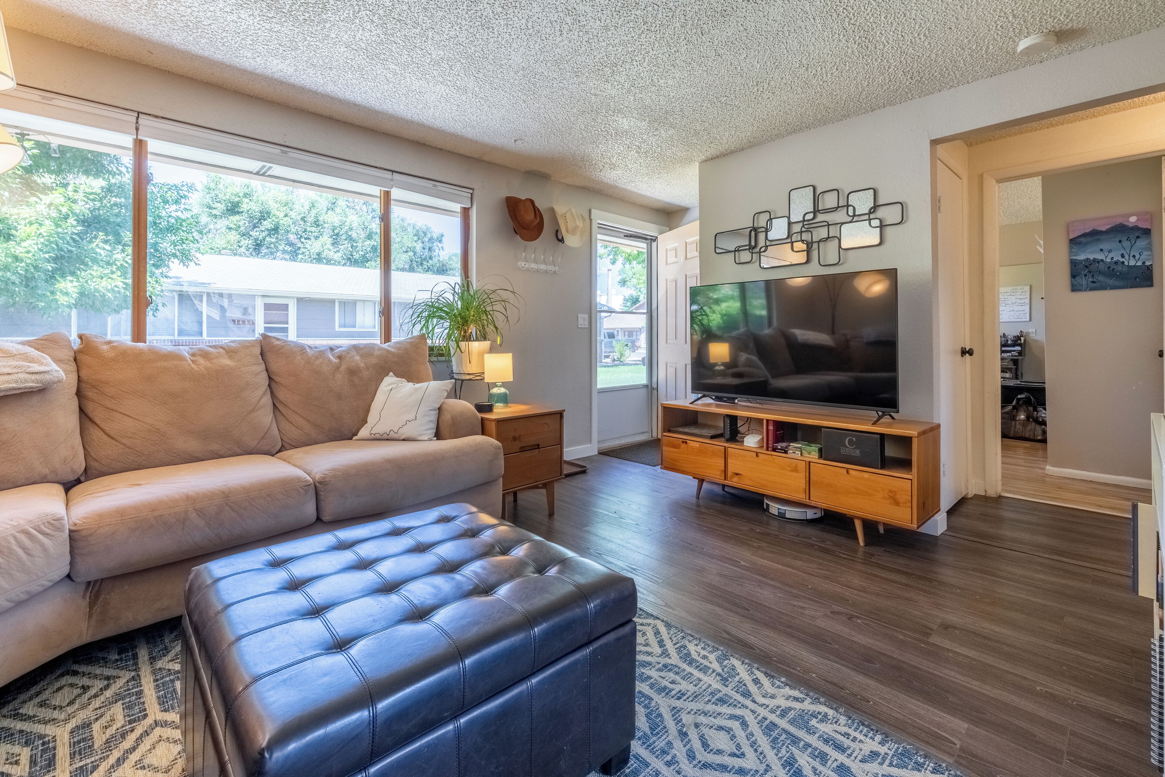 Un salon moderne avec un canapé en cuir, un pouf capitonné, un meuble TV en bois et un grand téléviseur à écran plat.