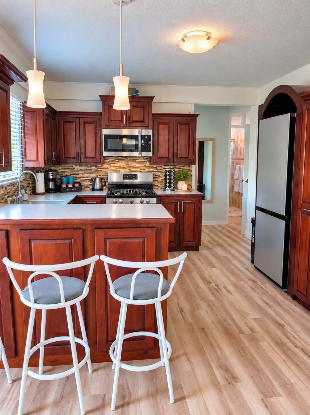 A kitchen with wooden cabinets, a central island with stools, a stainless steel refrigerator, and a microwave.