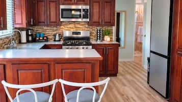 A kitchen with wooden cabinets, a central island with stools, a stainless steel refrigerator, and a microwave.