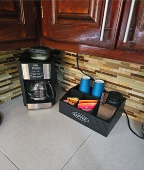 Una cafetera y una estación de café con tazas y sobres de café Folgers.