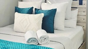 A neatly made bed with white and teal bedding, a teal throw blanket, and rolled white towels. - Entire rental unit in Calibishie, Dominica (Calibishie)