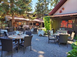 Un espace de restauration en plein air, avec des tables et des chaises, entouré d’arbres et bordé d’un bâtiment au toit rouge.