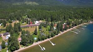 An aerial view of a lakeside property with houses, docks, and a forested mountain backdrop. - Laughing Horse Lodge (Bigfork)
