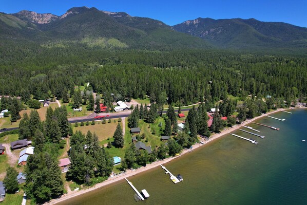 An aerial view of a lakeside property with houses, docks, and a forested mountain backdrop. - Laughing Horse Lodge (Bigfork)