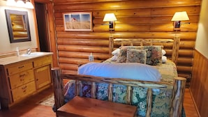 A wooden log cabin-style bedroom with a bed, bedside lamps, a wooden bench, a dresser, and a framed picture on the wall. - Laughing Horse Lodge (Bigfork)