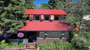 A two-story building with a red roof, a porch with green railings, and hanging flower baskets. - Laughing Horse Lodge (Bigfork)