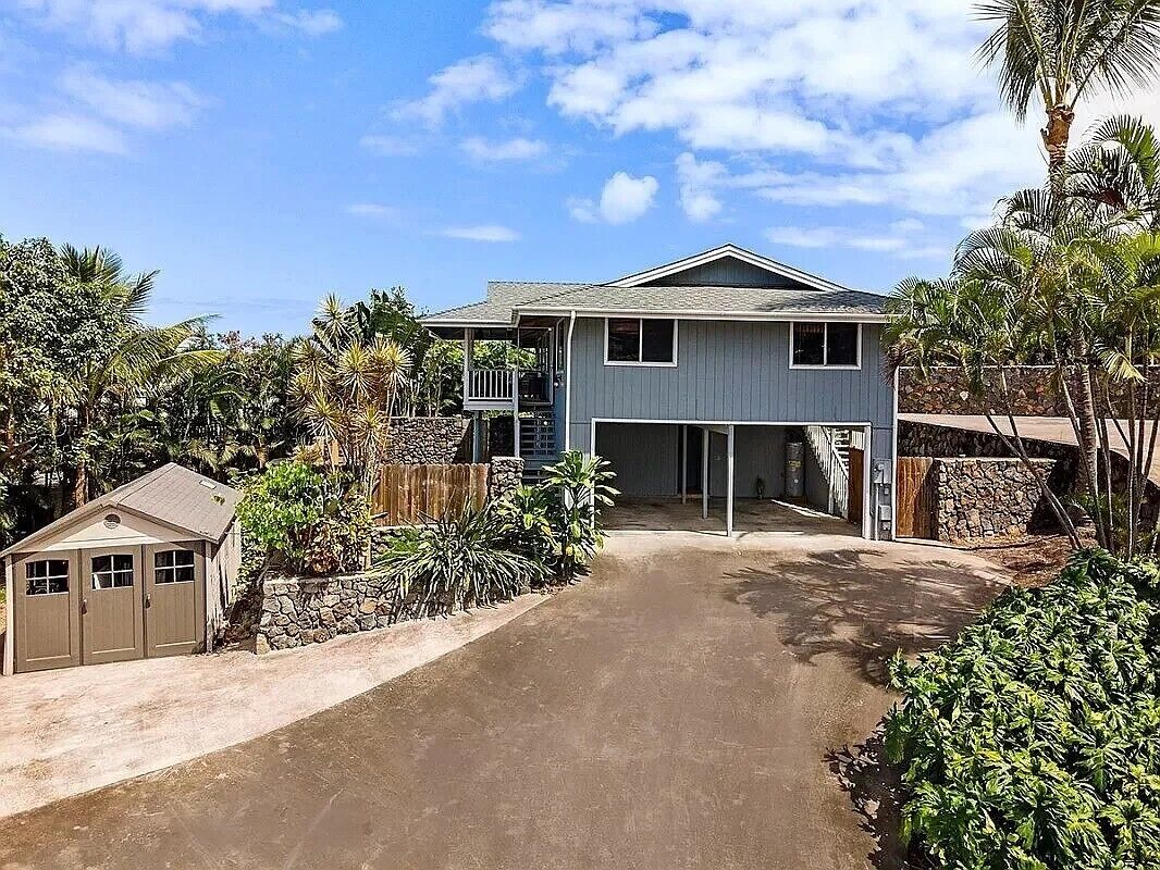 A two-story house with a garage, surrounded by tropical vegetation.