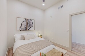 Une chambre à coucher avec un lit, deux œuvres d’art encadrées, une table de chevet avec une lampe et une porte.