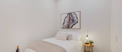 A bedroom with a bed, bedside table, and a wall-mounted artwork.