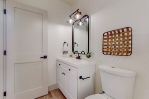 Een badkamer met een wit wastafel, spiegel en toilet. Er staat een klein plantje op de wastafel en er hangt een gevlochten mand aan de muur.