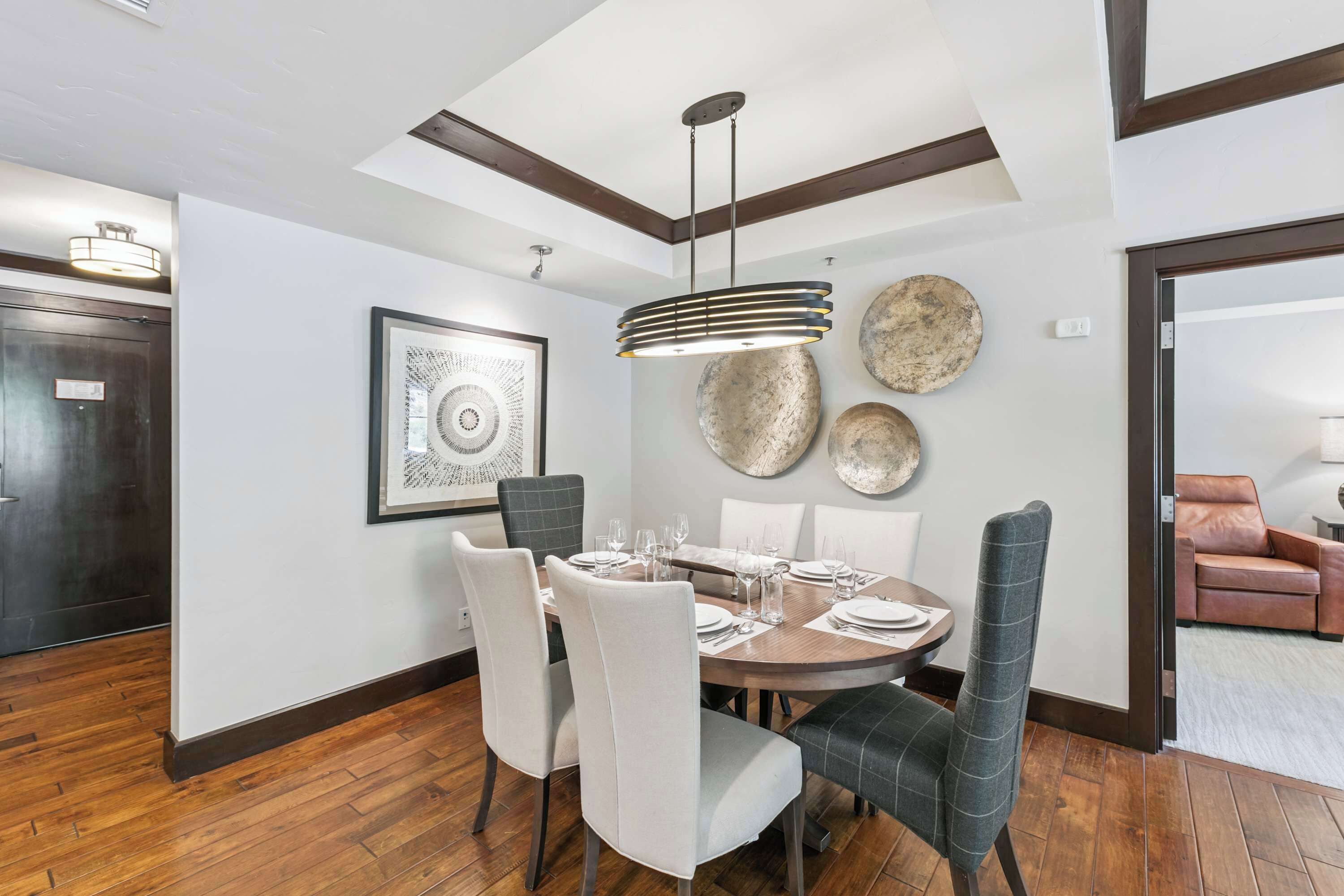 A dining area with a round table, chairs, a pendant light, and decorative plates on the wall.